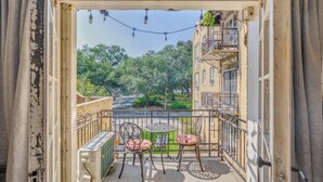 Un balcon avec deux chaises et une table, donnant sur une rue et sur de la verdure.