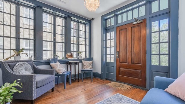 Une pièce dotée de grandes fenêtres, d’une porte en bois et d’un coin salon avec une table et des chaises.