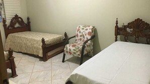 Ein Schlafzimmer mit zwei Betten, einem Sessel und einem Fenster mit Jalousien.