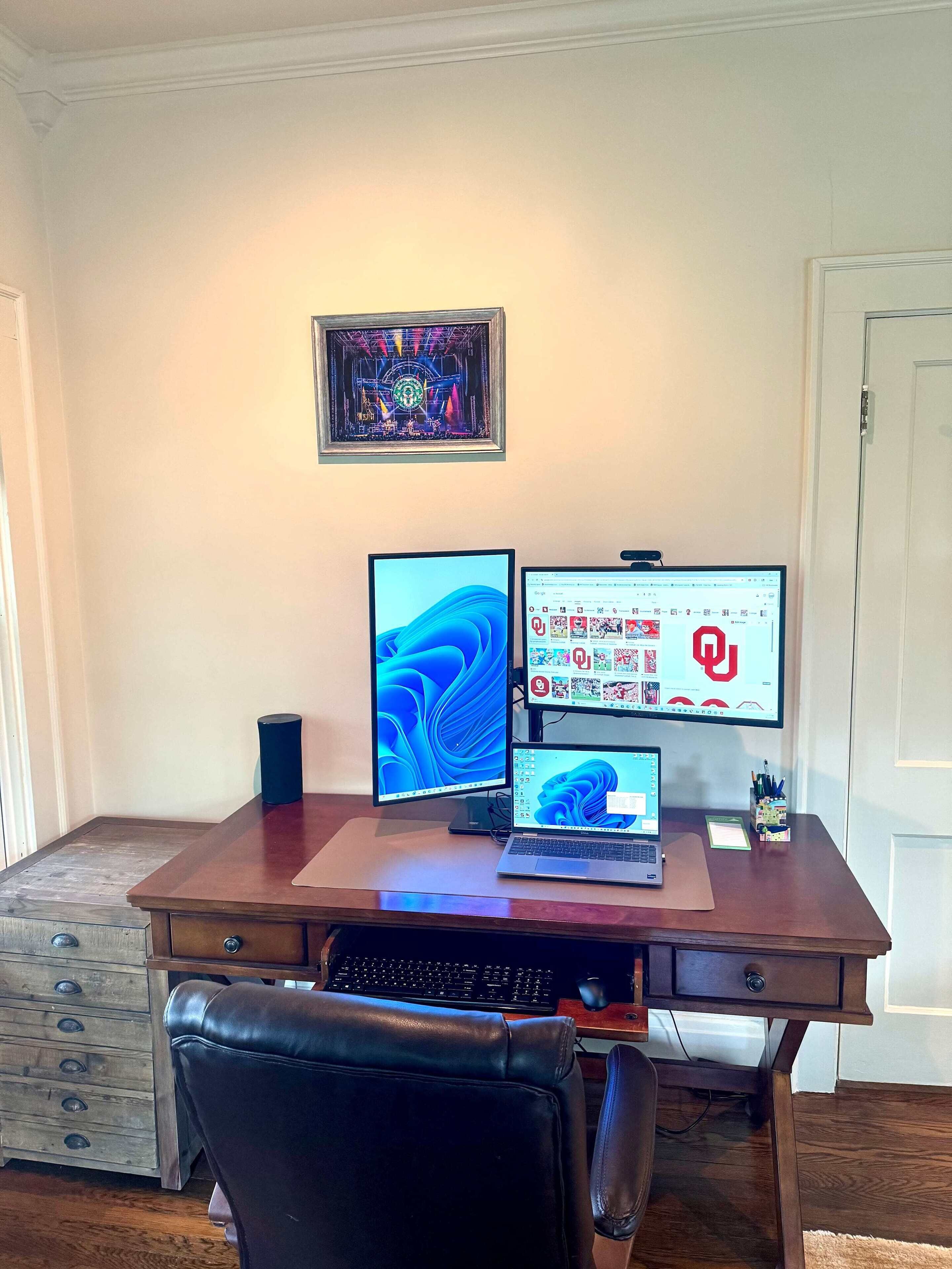Uma secretária de madeira com um laptop, dois monitores, um teclado e um rato.