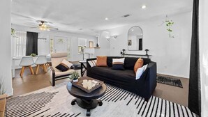 A modern living room with a black sofa, a coffee table, and a dining area with a table and chairs. - Stunning Lake Travis Retreat in Austin (Austin)