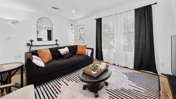 A modern living room with a black sofa, a round coffee table, and a large mirror on the wall. - Stunning Lake Travis Retreat in Austin (Austin)