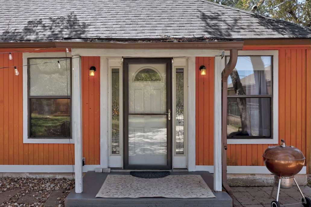 Une maison avec une porte d’entrée, deux fenêtres de chaque côté et un barbecue à l’extérieur.