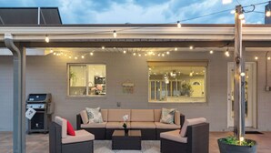 A covered outdoor seating area with a sofa, a coffee table, and string lights. - Spacious Scottsdale Retreat with Pool (Tempe)