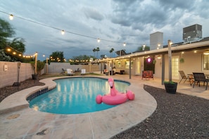 A swimming pool with a pink flamingo float, string lights, and a covered patio area. - Spacious Scottsdale Retreat with Pool (Tempe)