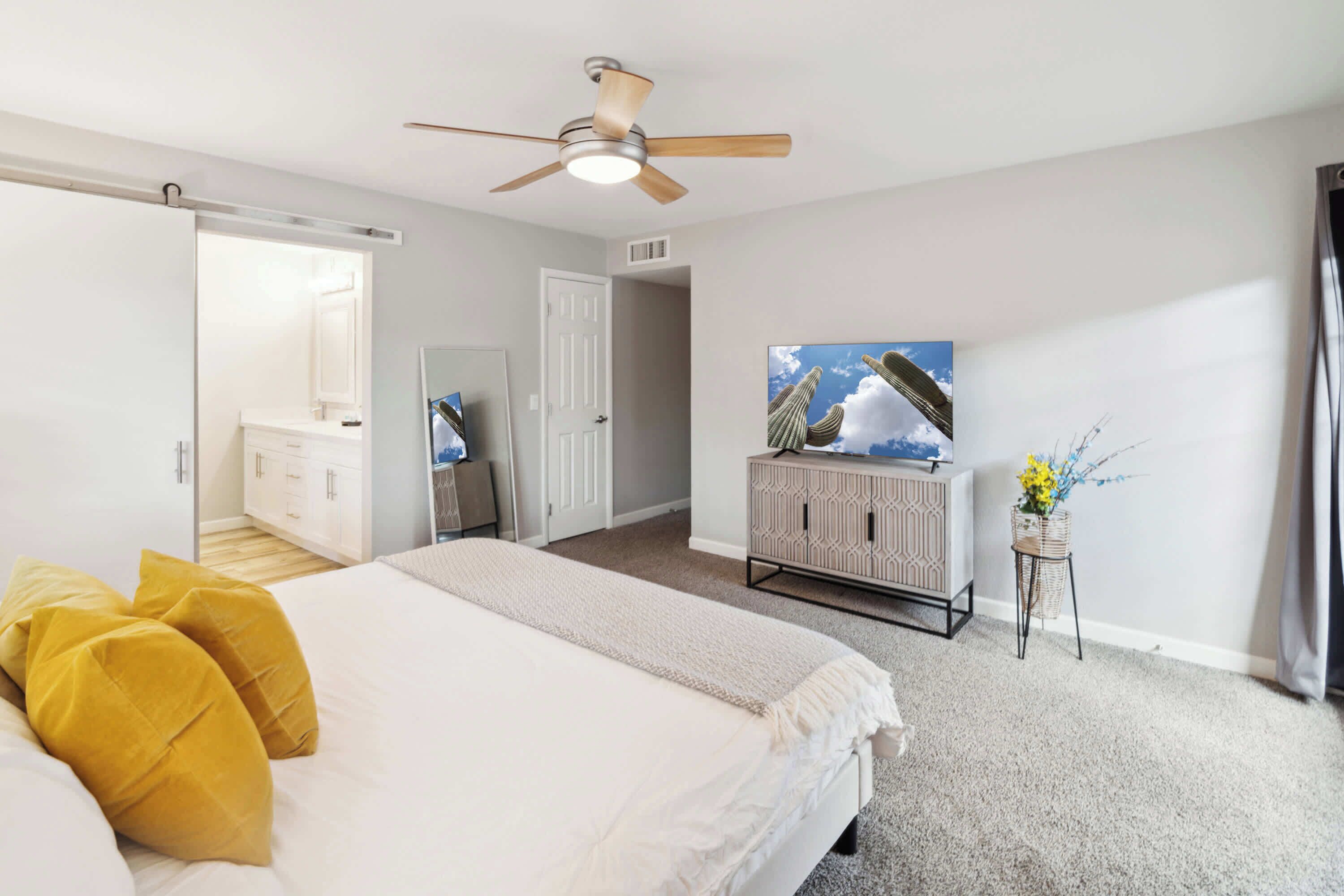 A bedroom with a bed, a ceiling fan, a dresser, a television, and a door leading to another room.