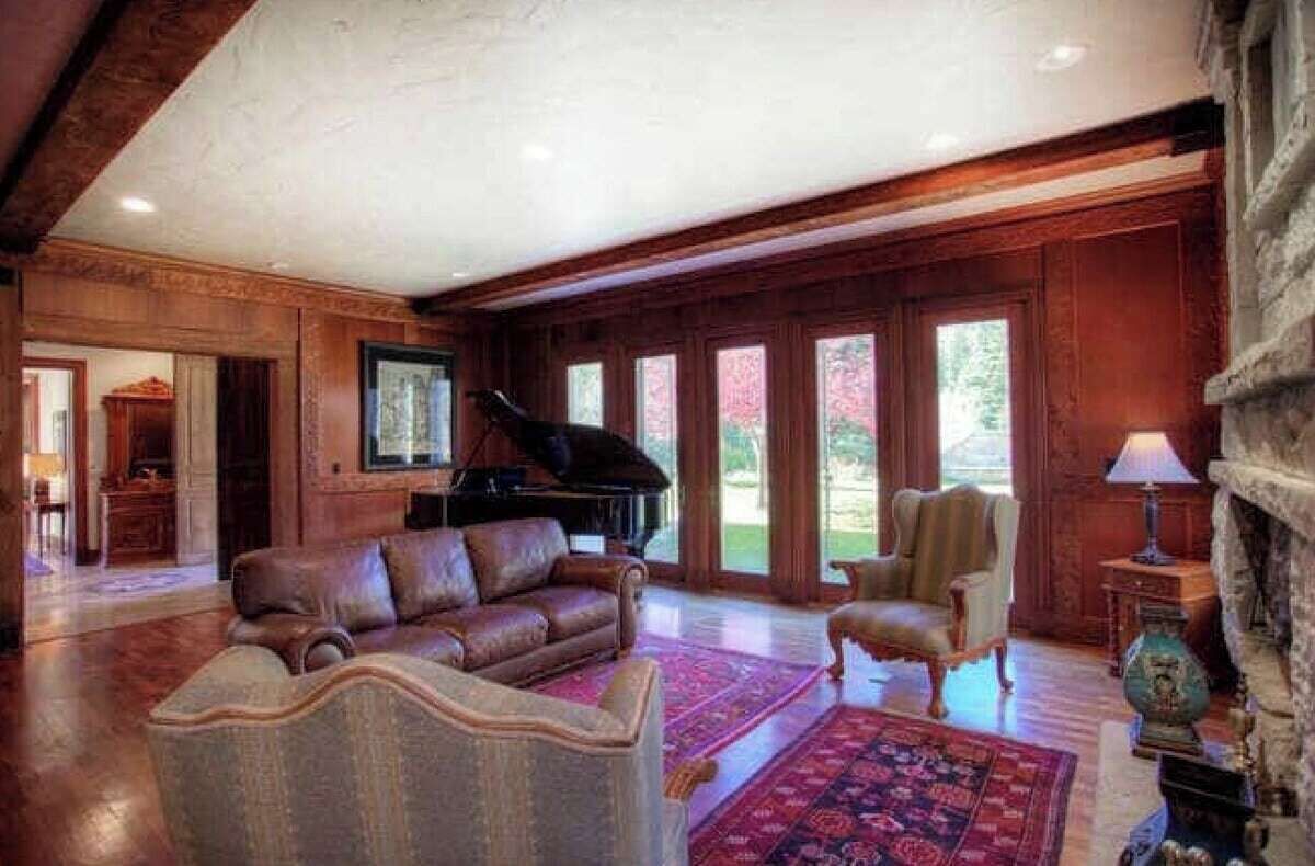 A spacious living room with a grand piano, leather sofa, and a stone fireplace.