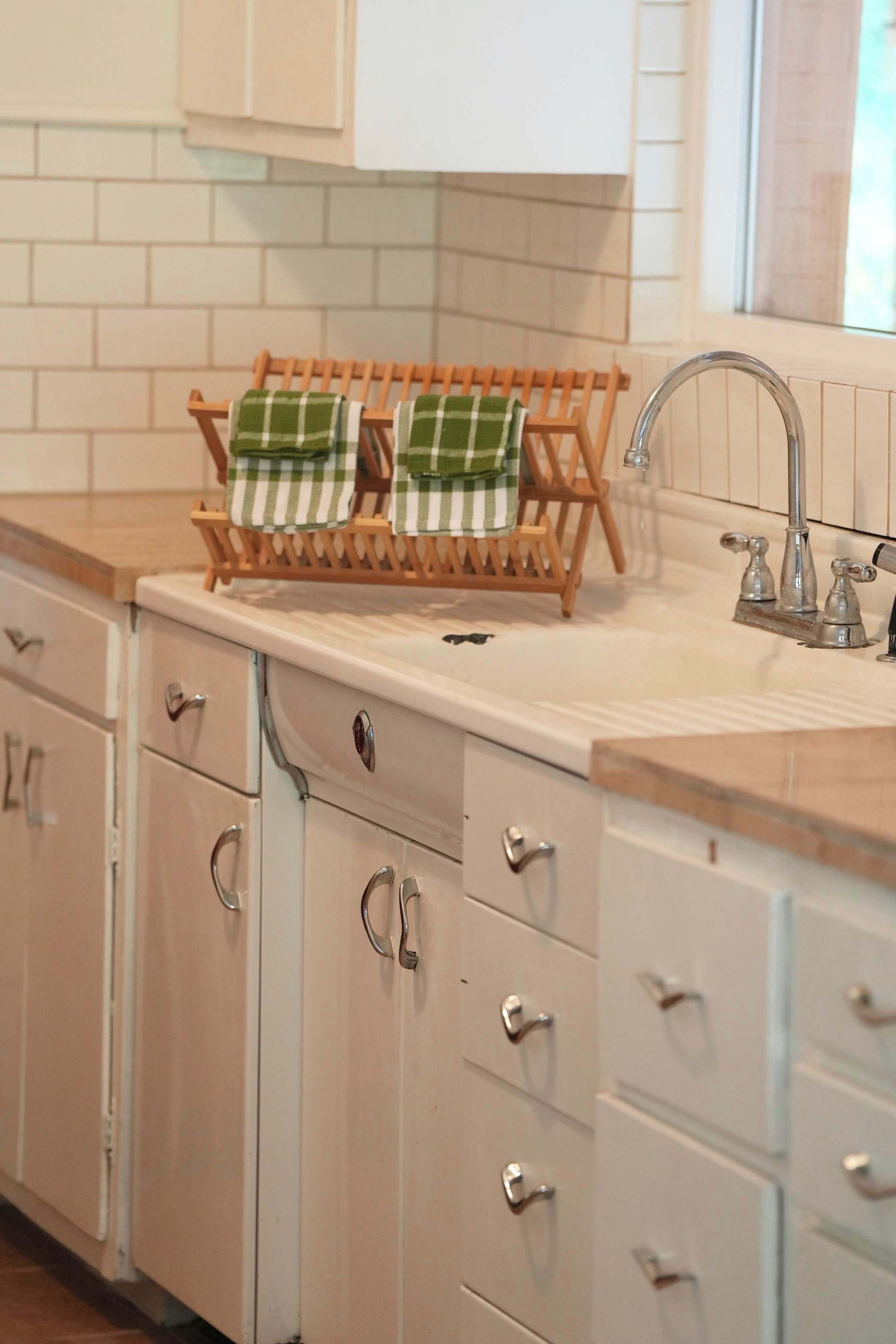 A kitchen with white cabinets, a wooden drying rack, and a stainless steel sink.