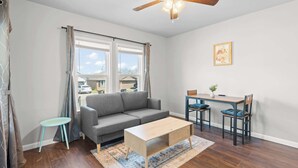 A living room with a gray sofa, a wooden coffee table, a small blue stool, and a dining table with two chairs. - Charming 1-Bedroom Retreat in Fort Worth (Fort Worth)
