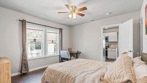 A bedroom with a bed, a ceiling fan, a window with curtains, and a door leading to a kitchen. - Charming 1-Bedroom Retreat in Fort Worth (Fort Worth)