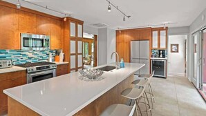 Una cucina moderna con mobili in legno, un'isola grande con sgabelli da bar, elettrodomestici in acciaio inossidabile e una parete di fondo rivestita di piastrelle blu e bianche.