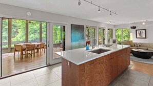 Una cucina moderna con un'isola grande, porte scorrevoli in vetro che conducono a una sala da pranzo e vista su spazi verdi esterni.