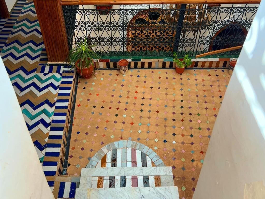 A courtyard with a patterned floor, a metal fence, and potted plants.