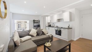 Een moderne woonkamer met een bank, een salontafel, en een keuken met witte kasten en apparatuur.