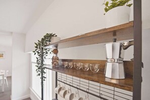 A kitchen with a wooden shelf, a coffee maker, and hanging mugs.