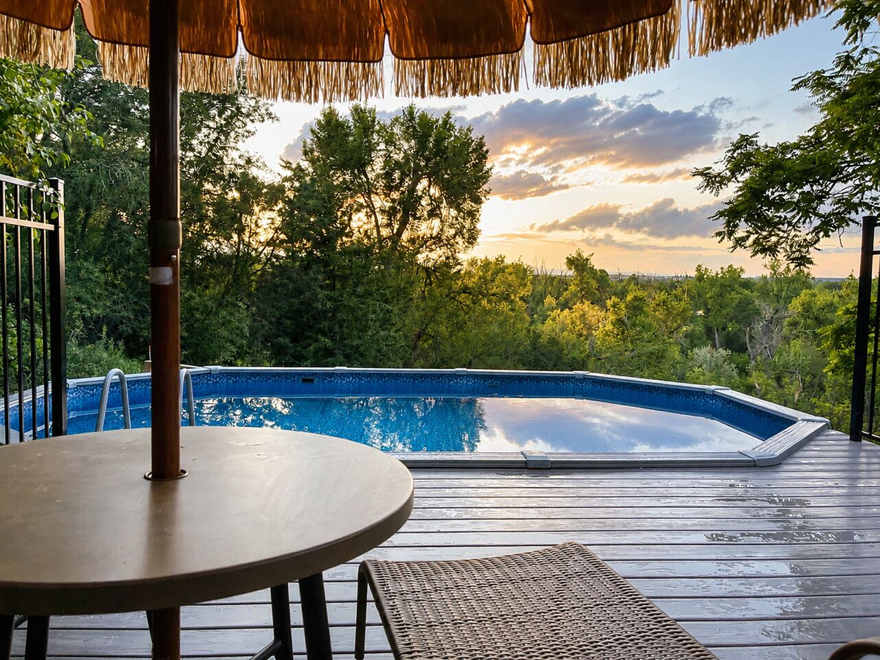 Une terrasse en bois avec une piscine, une table et un parasol en chaume.