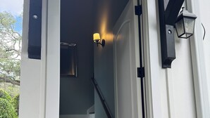 Una escalera con paredes blancas y peldaños de madera oscura que conducen a una puerta con marco de metal negro.