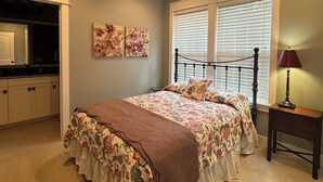 Un dormitorio con cama, ventilador de techo, ventana con persianas, mesita de noche y lámpara.
