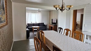 A dining area with a long table and wooden chairs, a sofa, and a television in the background. - 8 Person Holiday Home in Ryssby (Ryssby)