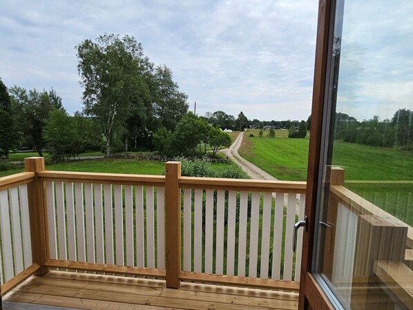 A wooden deck with a railing, overlooking a grassy field and trees. - 8 Person Holiday Home in Ryssby (Ryssby)