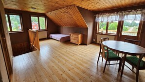 A room with a sloped ceiling, wooden floors, a bed, a dresser, a table with chairs, and large windows with curtains. - 8 Person Holiday Home in Ryssby (Ryssby)
