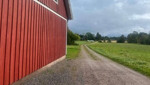 A red barn with a gravel path leading to a green field. - 8 Person Holiday Home in Ryssby (Ryssby)