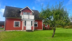 A red two-story house with a balcony, a small front porch, and a well-maintained lawn. - 8 Person Holiday Home in Ryssby (Ryssby)