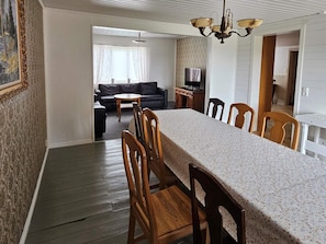 A dining area with a long table and chairs, a sofa, and a television in the background. - 8 Person Holiday Home in Ryssby (Ryssby)