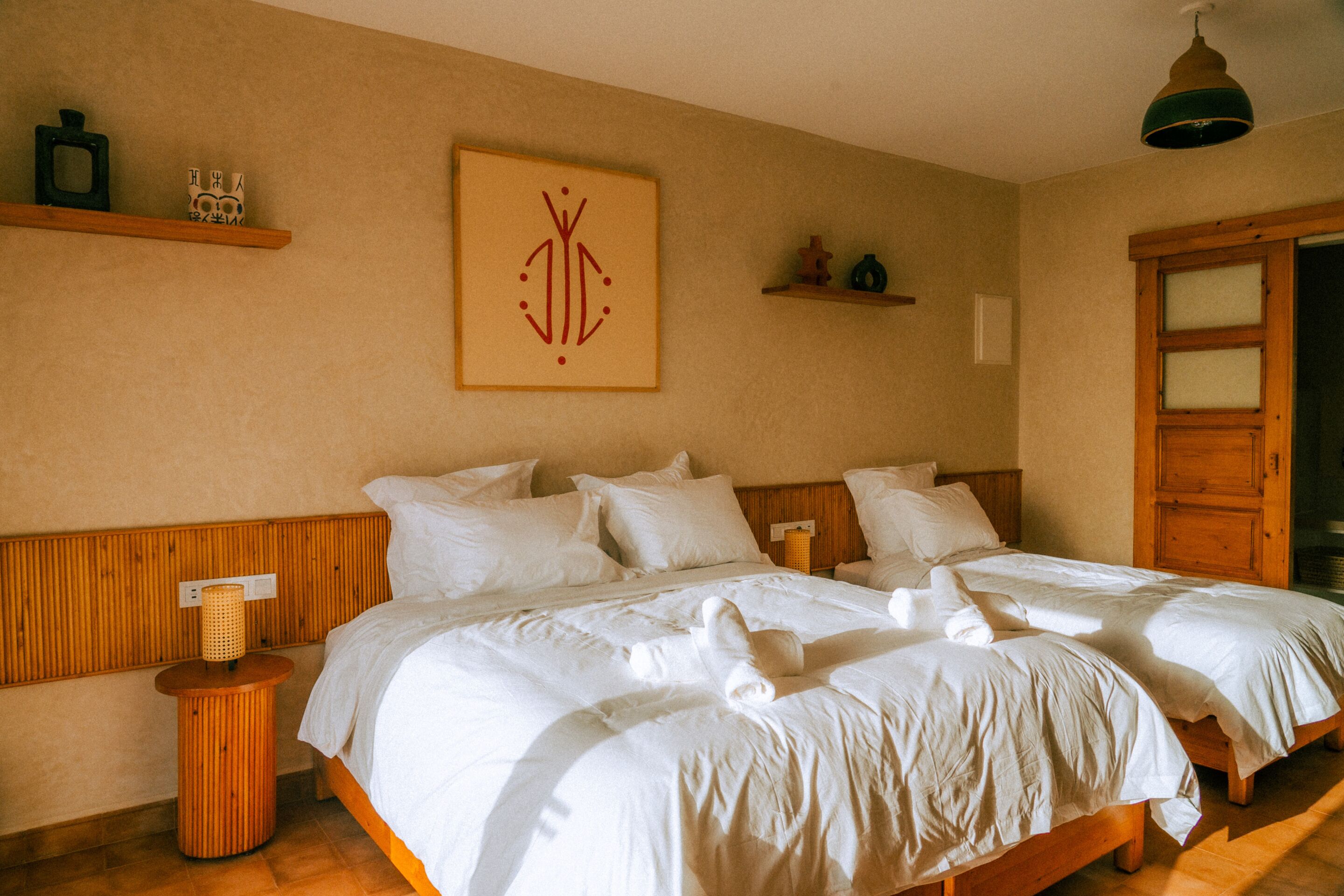 Une chambre d’hôtel avec deux lits, une tête de lit en bois, une table de chevet avec une lampe et une œuvre d’art encadrée au mur.