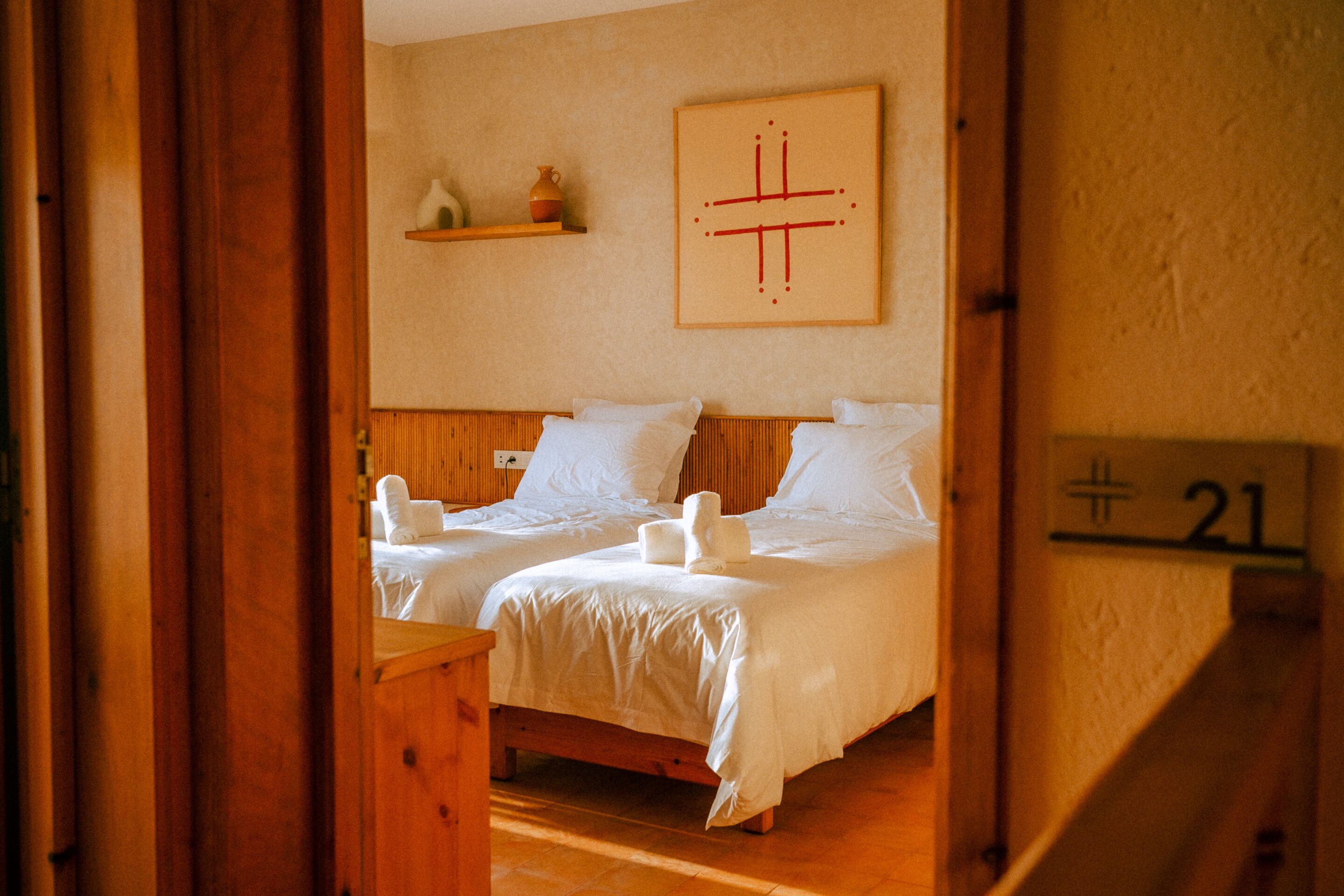 Una habitación con dos camas, piso de madera, un estante empotrado con objetos decorativos y un letrero con número en la pared.