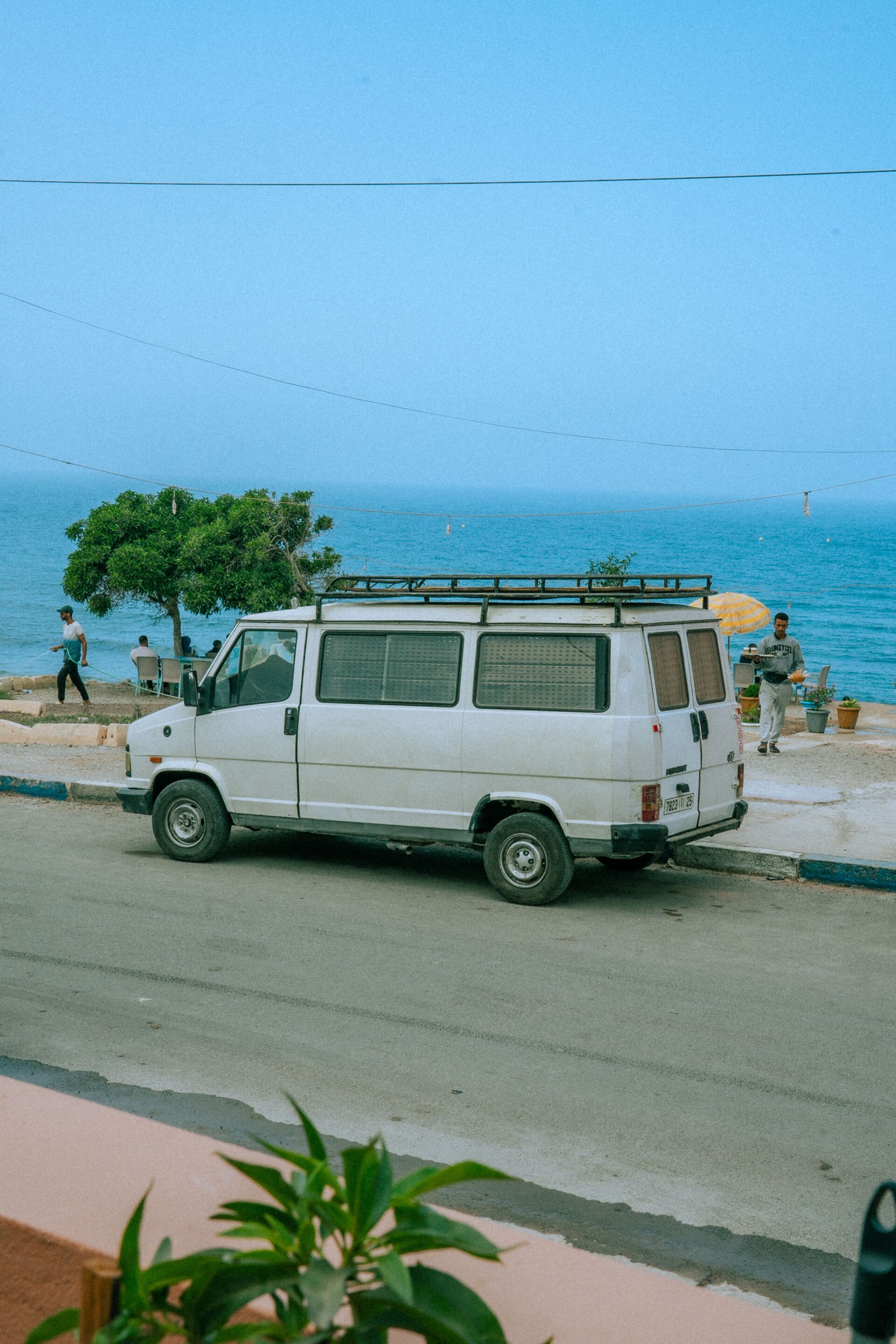 Un fourgon blanc est garé au bord de la route, avec la mer en toile de fond.