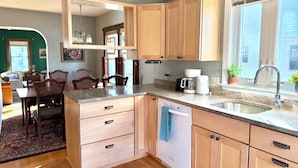 A modern kitchen with wooden cabinets, a granite countertop, a coffee maker, and a dishwasher. - Brunswick 3BR Bungalow By Bowdoin With Fenced-In Backyard (Brunswick)