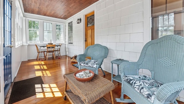 A cozy room with wooden flooring, wicker furniture, and a white brick wall. - Brunswick 3BR Bungalow By Bowdoin With Fenced-In Backyard (Brunswick)