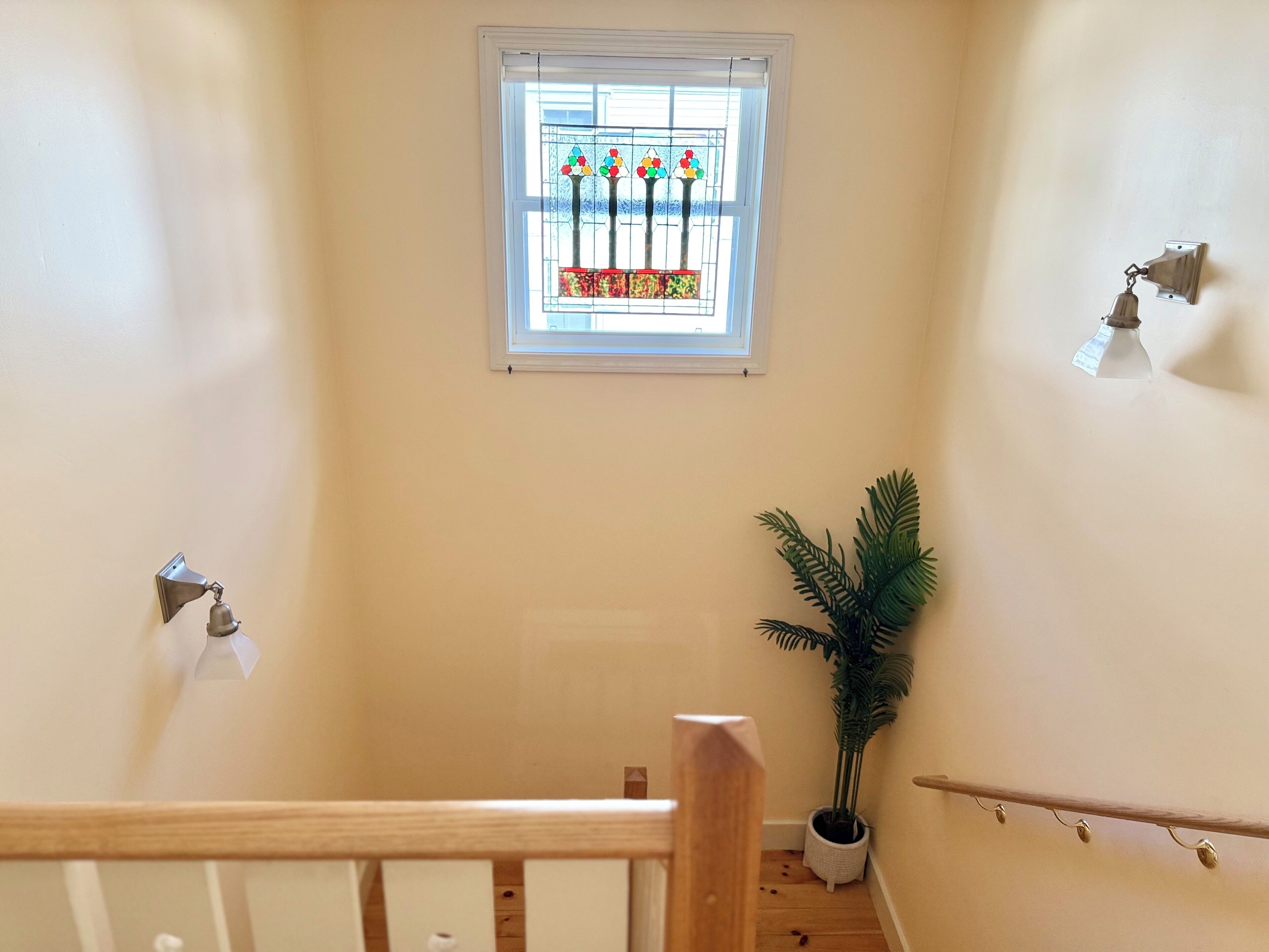 Un escalier avec une rampe en bois, une plante en pot, une fenêtre à vitraux et un luminaire fixé au mur.