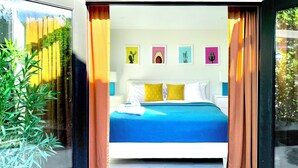 Una camera d'albergo moderna con un letto grande, una finestra con tende e opere d'arte alle pareti.