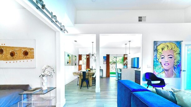 Un soggiorno moderno con un divano blu, una zona pranzo con tavolo in legno e un angolo cucina con televisore.