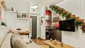 Un soggiorno moderno con divano, tavolo in legno, televisore e angolo cottura con piastrelle rosse.