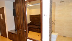 A hotel room with a wooden wardrobe, a bed with a headboard, a toilet, and a shower area. - BAGA RESIDENCY (Calangute)