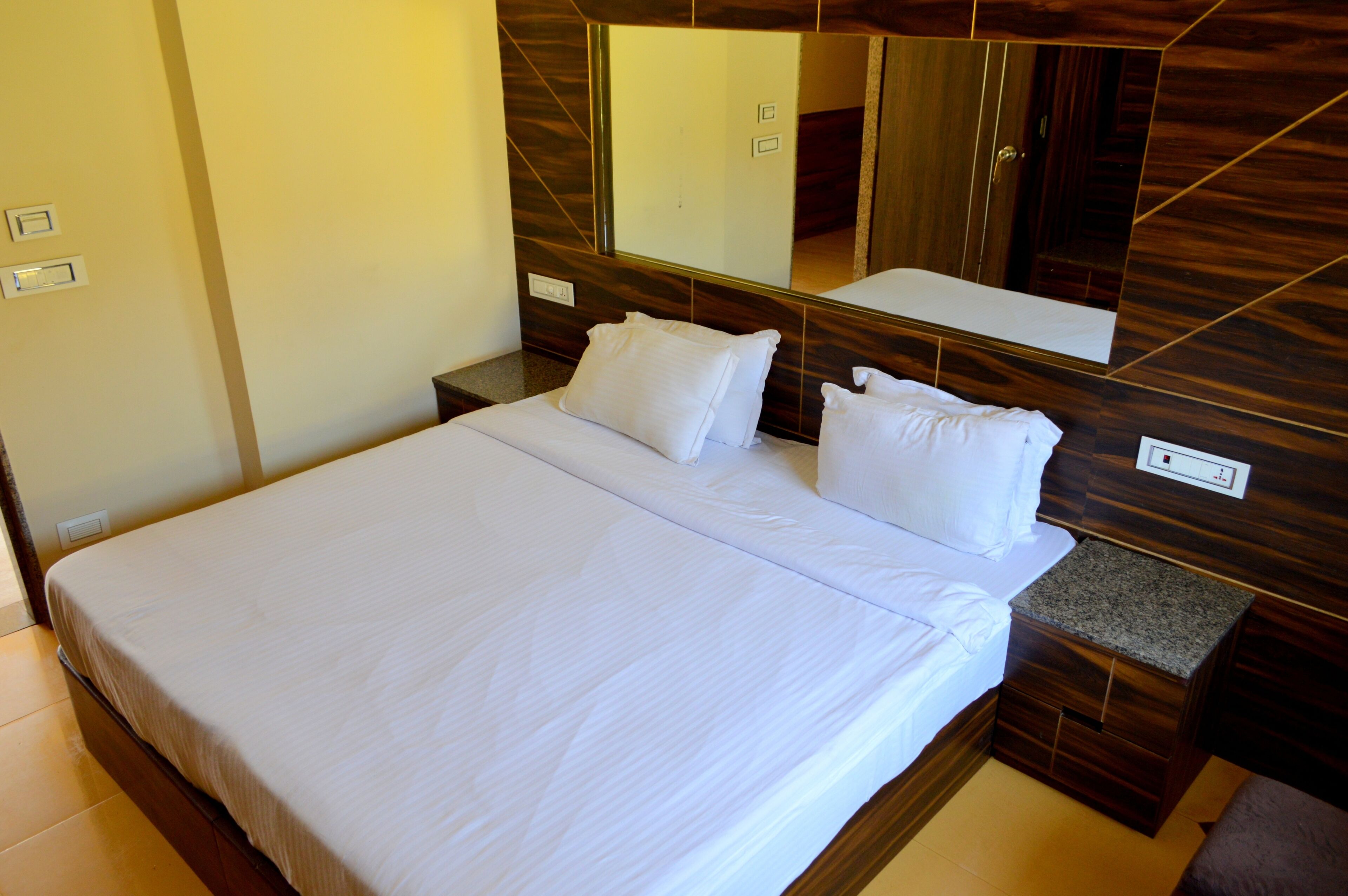 A hotel room with a large bed, a wooden headboard, a nightstand, and a mirror.