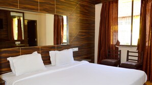 A large bed with white linens, a wooden headboard, a large mirror, and a window with curtains. - BAGA RESIDENCY (Calangute)