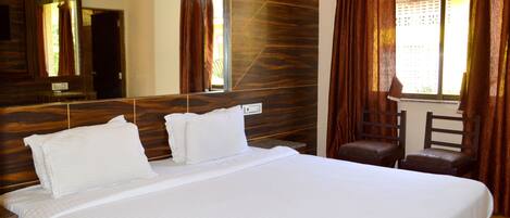 Una cama grande con ropa de cama blanca, un cabecero de madera, un espejo grande y una ventana con cortinas.