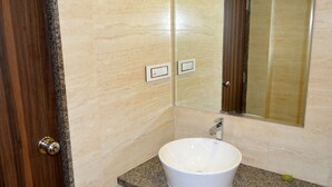 A bathroom with a marble wall, a wooden door, a white sink, and a mirror. - BAGA RESIDENCY (Calangute)
