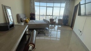 Una camera da letto moderna con un letto grande, una scrivania e vista sulla città attraverso ampie finestre.