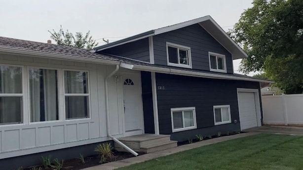 A two-story house with a garage, a front porch, and a small front yard. - Lumi Deluxe (Saskatoon)