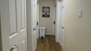 A hallway with white doors, a trash can, and a picture of the Eiffel Tower on the wall. - Lumi Deluxe (Saskatoon)