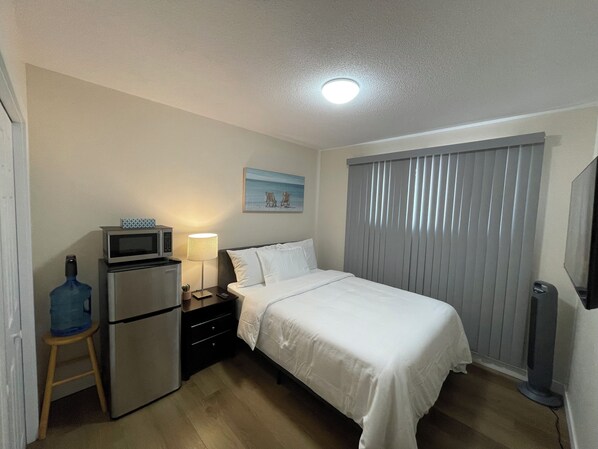 A hotel room with a bed, a desk with a lamp, a refrigerator, a microwave, and a picture on the wall. - Lumi Deluxe (Saskatoon)
