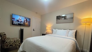 A hotel room with a large bed, a TV mounted on the wall, a chair, a lamp, and a painting. - Lumi Deluxe (Saskatoon)