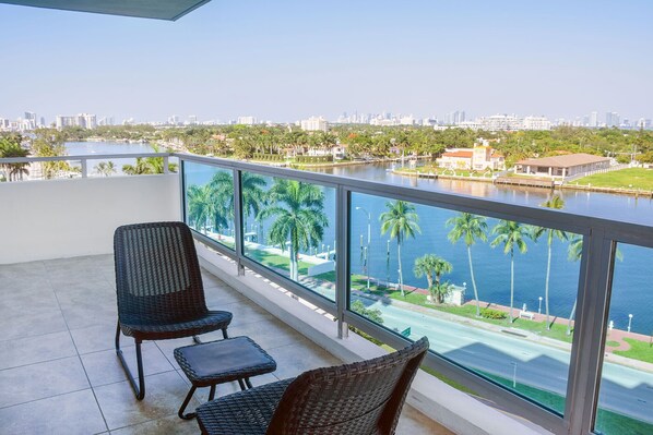 A balcony with wicker chairs and a view of a cityscape across a river.