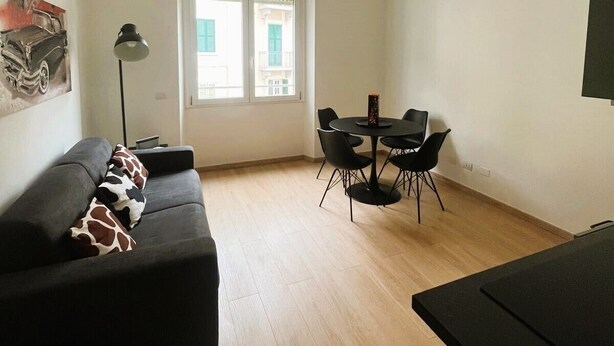 A living room with a black sofa, a dining table with chairs, a lamp, and a ceiling light. - Casa Sforza - stylish apartment in the heart of Bergamo! (Bergamo)