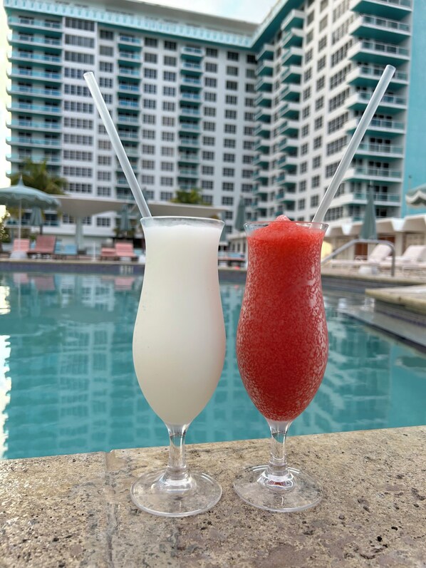 Two drinks on a poolside table with a hotel in the background.